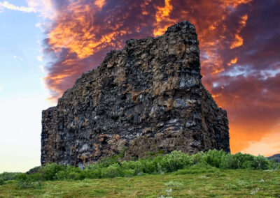 A massive rock structure rises from a vibrant grassy field, creating a striking natural landmark.