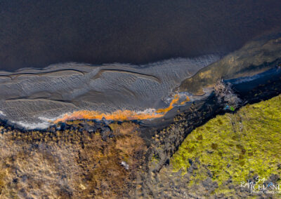 Overhead shot of Iceland's black sand beach, featuring striking orange water that creates a unique coastal landscape.