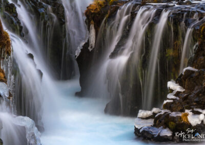 A majestic waterfall flows down a rocky cliff in Iceland, highlighting the dramatic scenery of the region.