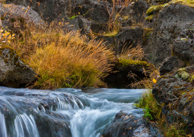 A majestic waterfall flows over rocks, highlighting the Autumns colors serene wilderness of Iceland.