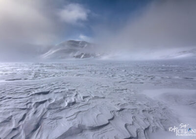 A tranquil winter scene showcasing a snow-covered terrain with a prominent mountain towering in the distance in Iceland