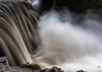 A stunning Icelandic waterfall cascades gracefully in the foreground, with water flowing over rocky cliffs.