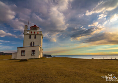 A lighthouse perched on a hill in Iceland, overlooking the vast ocean under the evening colorful sky.