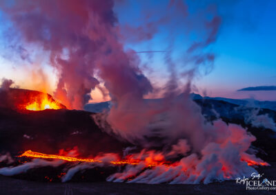 A volcano erupts, with molten lava flowing down its sides, set against a stunning sunset sky in Iceland