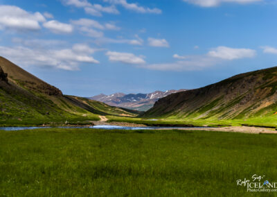 An Icelandic valley showcasing a serene river surrounded by impressive mountains in the background.