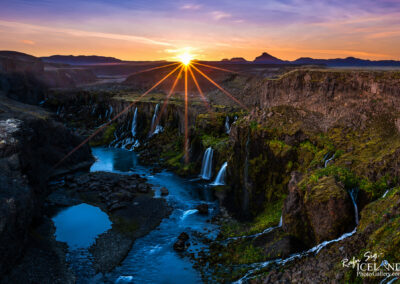 The sun sets dramatically over a stunning Icelandic waterfall, illuminating the landscape with warm hues and tranquil beauty.