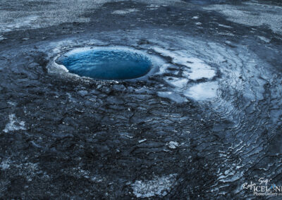 A geothermal site in Iceland featuring a hole in the ground with clear blue water, emphasizing its natural beauty.