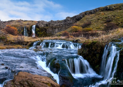 Majestic waterfalls cascading down rocky cliffs in Iceland, surrounded by lush greenery and dramatic landscapes.