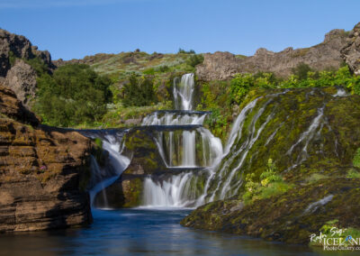 A stunning waterfall in Iceland, flowing powerfully over Lava rocks, creating a misty atmosphere and vibrant landscape under a blue sky