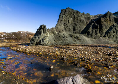 Majestic Icelandic mountain with rugged rocks and a tranquil water body in the foreground, showcasing natural beauty.