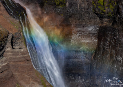 A vibrant rainbow inside a waterfall in Iceland, creating a stunning natural view against the colorful rocks.