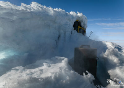 A mountain in Iceland adorned with a large snow pile, featuring a cabin and a glacier in the picturesque scenery.