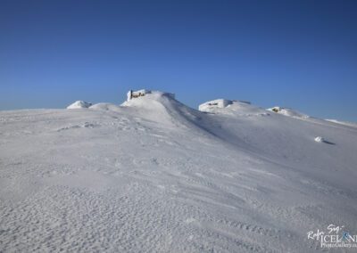 Snow-covered mountain in Iceland under a clear blue sky, with cozy cabins nestled at the top of the Glacier.