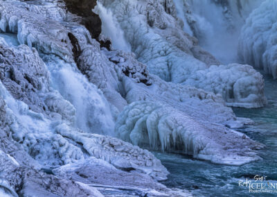 Chunks of ice tumble into the water beneath a waterfall, showcasing the dynamic interplay of ice and liquid.