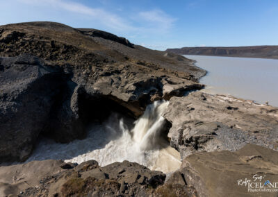 A stunning waterfall framed by a dramatic canyon landscape in Iceland comng from a a peaceful lake under a blue sky