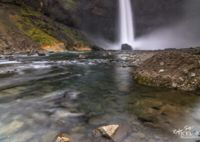 A majestic waterfall tumbles into a river, highlighting the serene beauty of Iceland's wilderness.