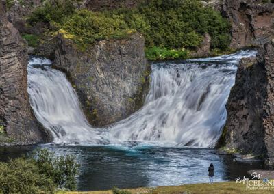 A person admires a powerful waterfall, with water flowing dramatically and mist creating a serene atmosphere around them.