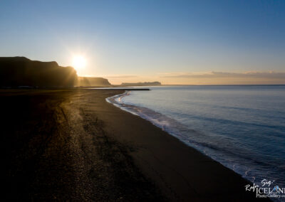 A picturesque sunset over the ocean, with the black beach bathed in golden light, evokes a sense of peace and serenity.