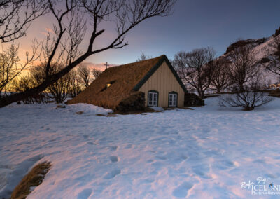 A charming small turf church in Iceland covered in snow, set against a peaceful winter backdrop in the colors of sunset.