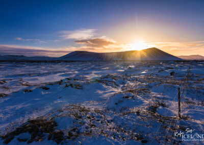 A stunning sunset casts warm hues over a snowy Icelandic field, framed by majestic volcano mountain in the background.