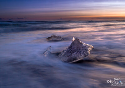 A rugged rock on the shoreline, bathed in the golden light of sunset, highlighting the peaceful black beach diamond atmosphere.