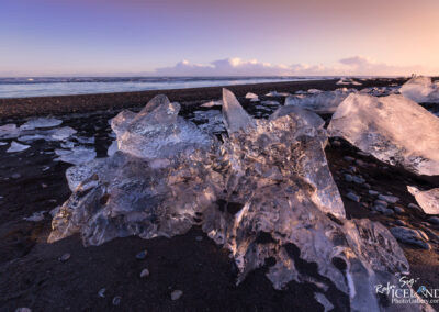 A serene black beach scene at sunset, featuring ice diamonds formations reflecting the vibrant colors of the sky.