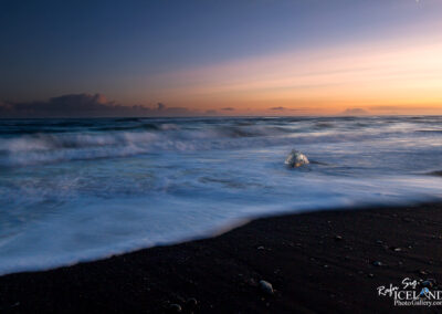 A single ice diamond stands on the black beach, surrounded by the vibrant colors of a sunset sky.