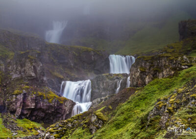 Fallegur þrepaskiptur foss þar sem þoka hylur efsta hlutann. Stallaður foss í Mjóafirði á Austurlandi