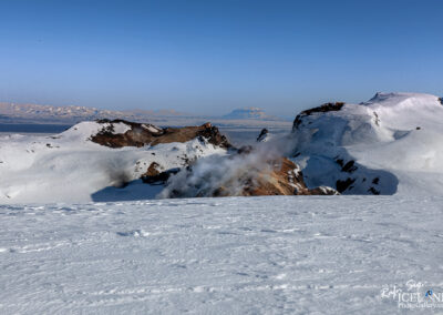 Geyser erupting from an Icelandic glacier under a clear blue sky in the highlands with mountain in the background.