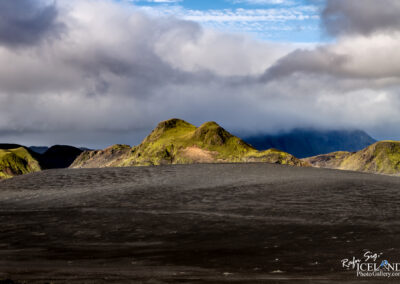 Black volcanic sand in the highlands of Iceland with dramatic mountains rising in the background, showcasing natural beauty.