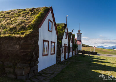 A charming old turf-house house with a church tower behind, showcasing traditional Icelandic architecture amidst the beautiful landscape.