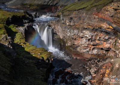 A picturesque waterfall in Iceland, complemented by a colorful rainbow stretching across the sky.