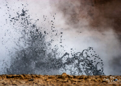 In front of a steaming mud Geyser, showcasing the rugged terrain of the Icelandic nature.