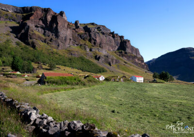 A grand rock wall featuring steep cliffs and varied surfaces, highlighting the beauty of natural geology and the old farm in the foreground