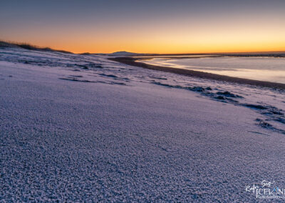 Quiet moment on a snow-covered black beach, with the calm sea and winter scenery creating a peaceful atmosphere and volcano in the background.