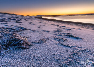 A serene frosty black beach at sunrise, with soft pastel colors illuminating the icy shoreline and gentle waves.