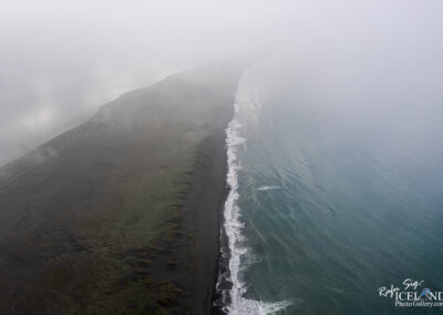 A tranquil black sand beach under a foggy sky, with soft ocean waves lapping at the shore.