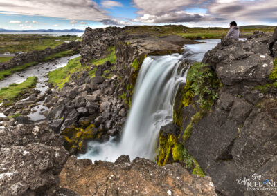 A picturesque waterfall in Iceland, flowing gracefully over rocks, framed by vibrant nature and rugged terrain.