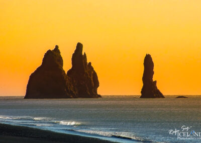 Three unique rock formations stand near the black beach, beautifully illuminated by the pastel yellow color of the sunrise.