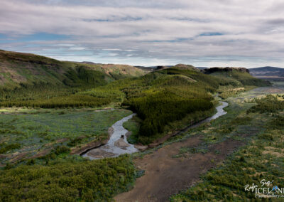 A winding river traverses a verdant valley, with stunning mountains rising prominently in the background.