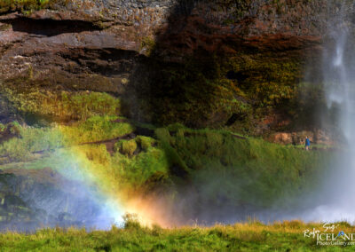 A brilliant rainbow appears above a waterfall, enhancing the picturesque landscape with its vivid colors.