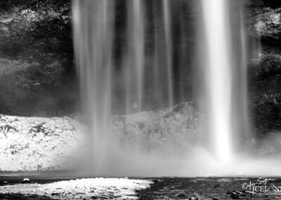 A serene black and white image capturing the cascading flow of a waterfall amidst a natural landscape.