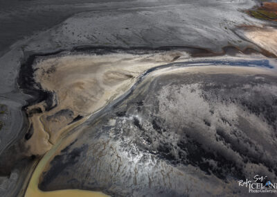 A river meanders through a black sandy and muddy terrain, highlighting the contrast between water and earth.