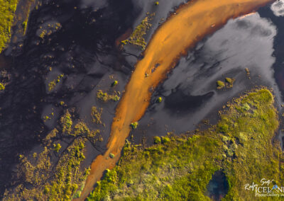 Bird's-eye view of a river featuring unusual orange water, set against a backdrop of rich green foliage.