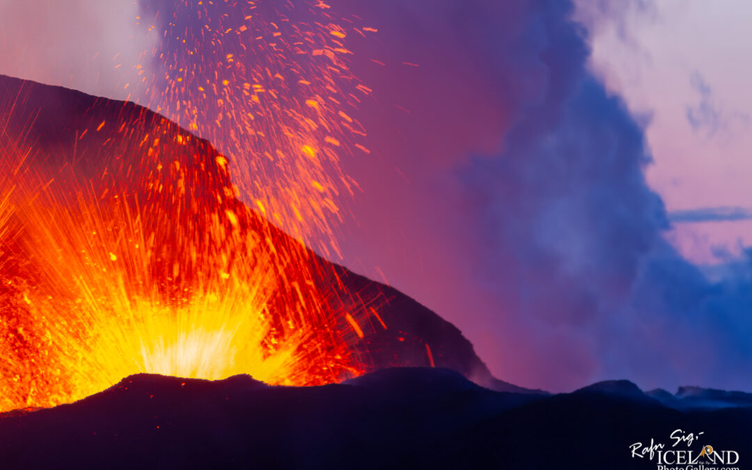 A vibrant eruption of a volcano, with bright orange and yellow lava bursting upwards against a backdrop of purple and dark clouds. The molten rock projects upwards, creating a dramatic and fiery display at the summit, while ash and smoke billow into the atmosphere. The surrounding landscape features dark volcanic soil.